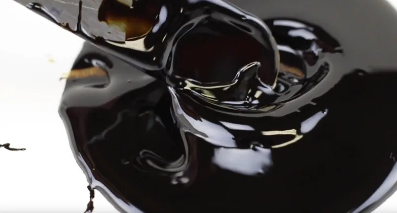 Dark open-gear fluid pooled around a blade, amber where the film thins.